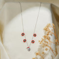 Silver necklace with four red and green beaded flowers and a crystal Santa pendant on cream fabric