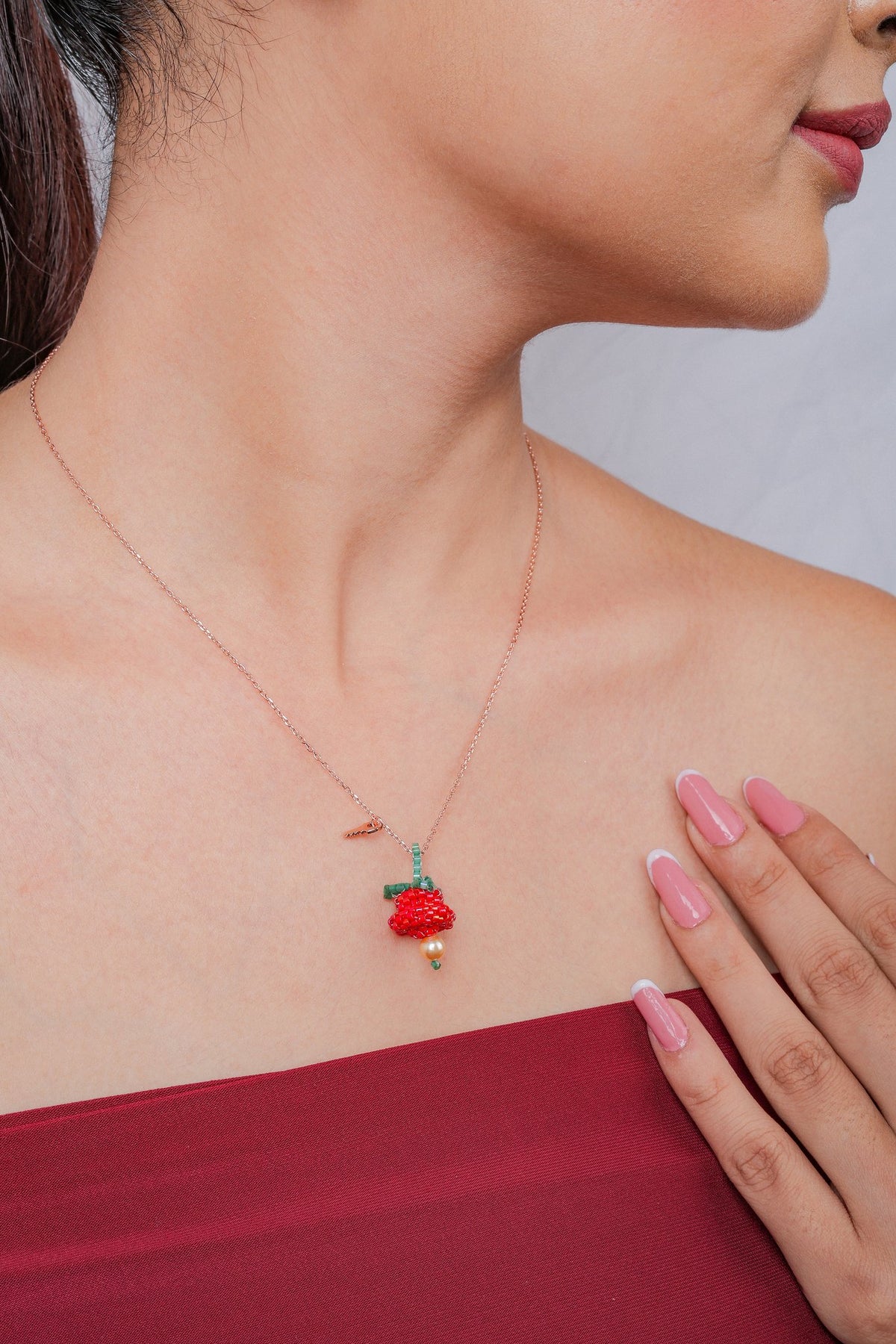 Rose-gold chain with a red beaded bloom pendant, green leaves, pearl-look drop and tiny key charm