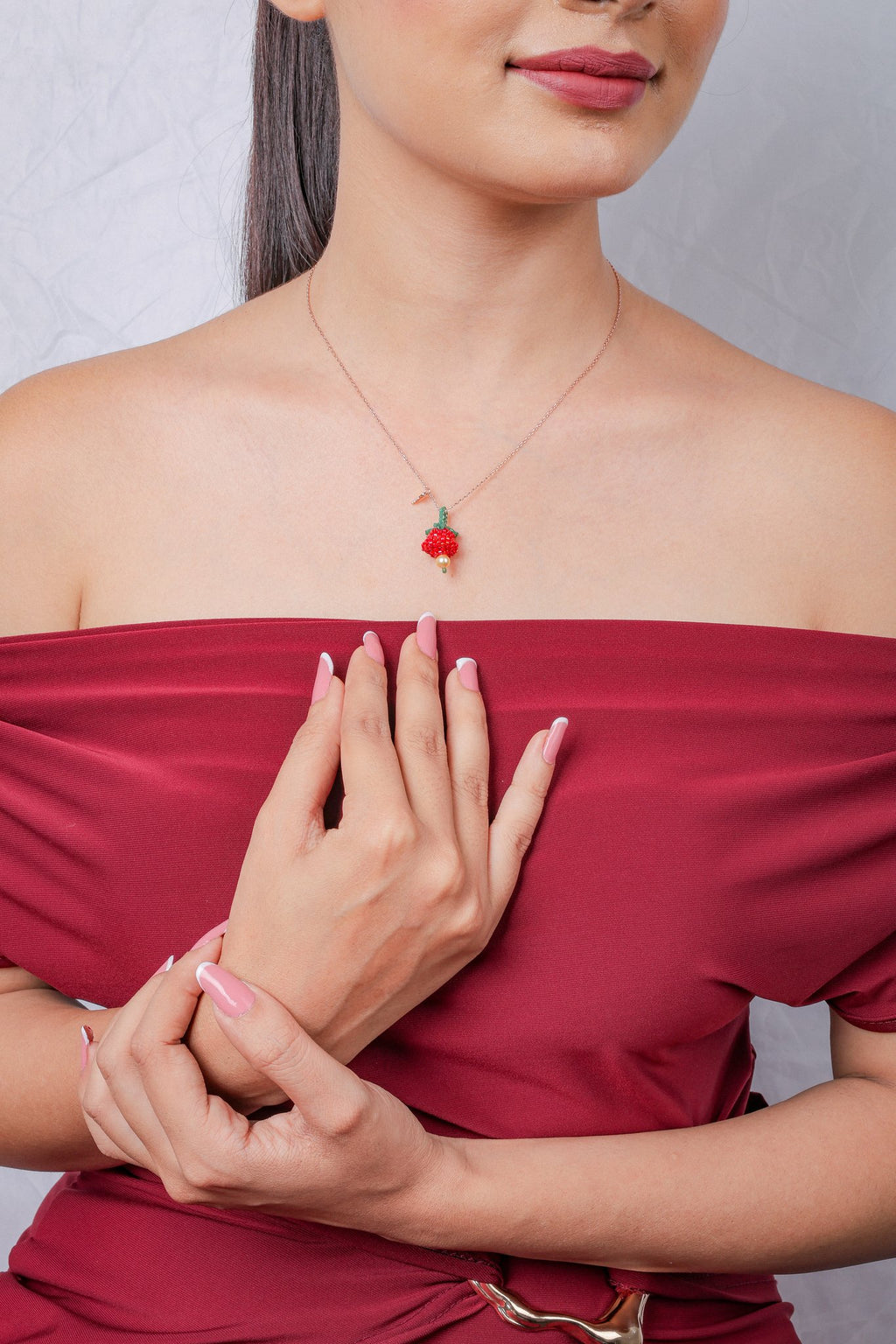 Model wearing rose-gold necklace with red beaded bloom pendant and small key charm