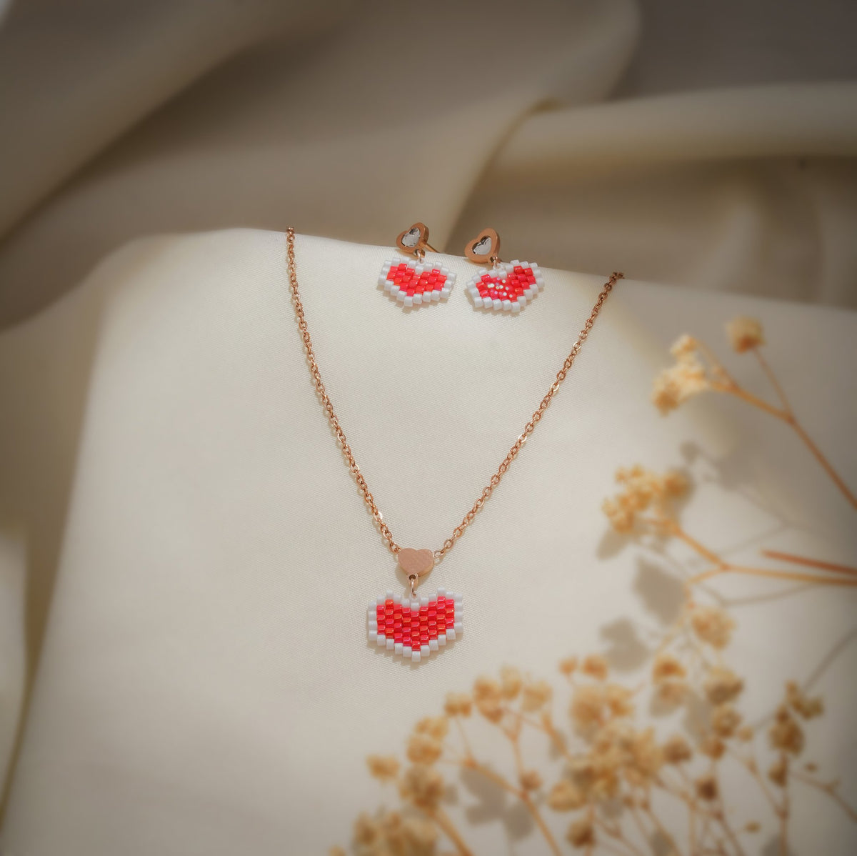 Rose-gold necklace with white-edged red beaded heart pendant and matching heart drop earrings on cream silk