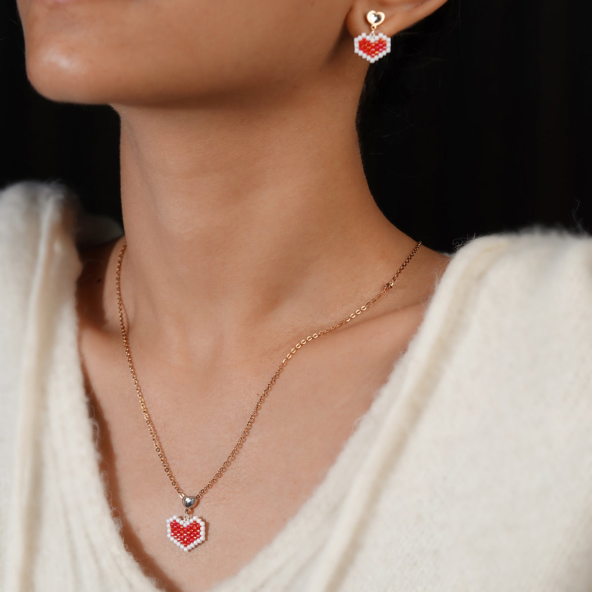 Model wearing the red beaded heart pendant on a rose-gold chain with matching heart drop earrings