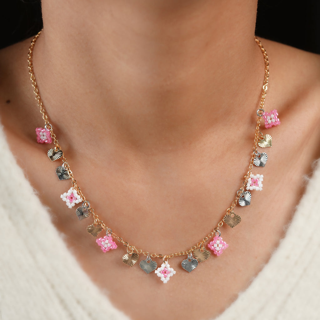 Model wearing the pink beaded square and two-tone heart charm necklace at the collarbone