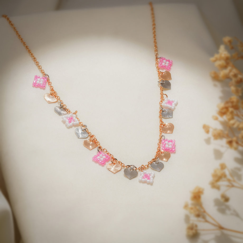 Pink and white beaded charms with textured heart charms on a rose-gold chain over cream fabric