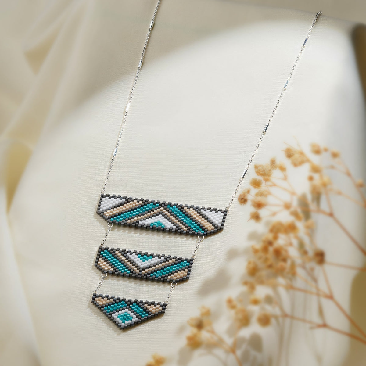 Silver chain necklace with three tiered beaded panels in teal, sand, white and grey chevrons