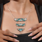 Model wearing silver necklace with tiered teal and sand chevron beaded pendant over a black top