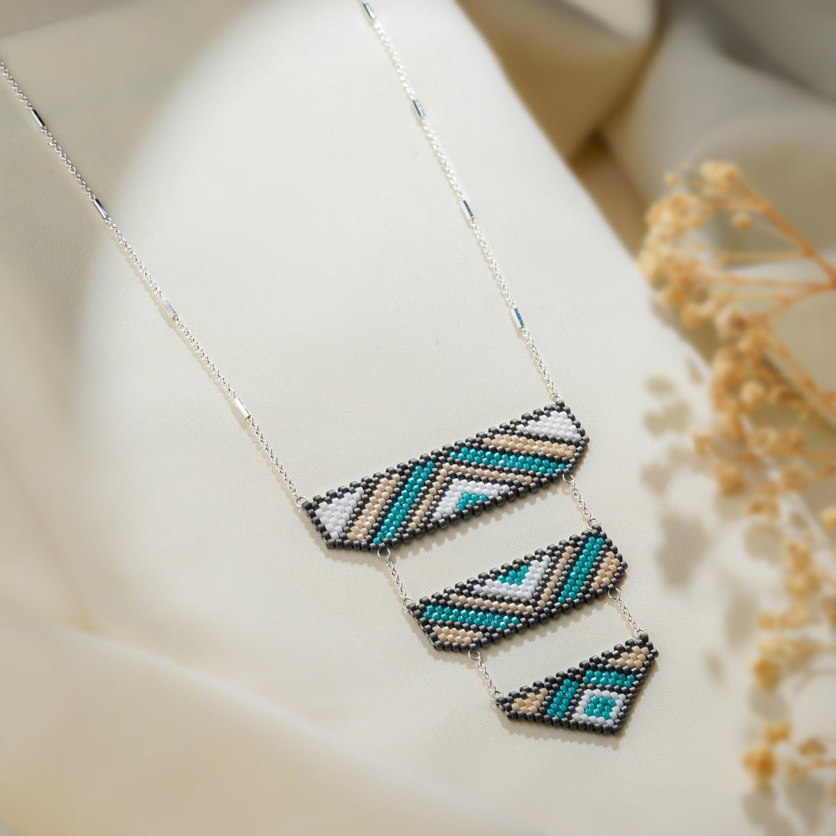 Angled view of three graduated beaded panels with teal diamond and chevron patterns on silver chain