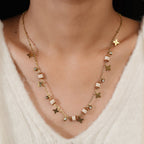 Model wearing gold necklace with beaded barrels, four-point star charms and crystal drops