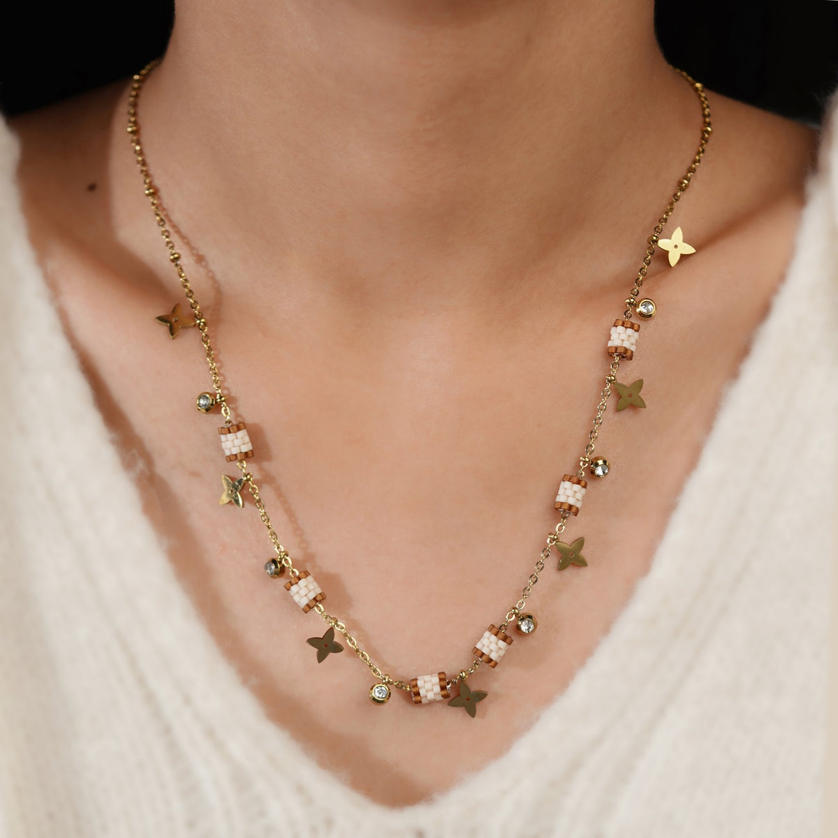Model wearing gold necklace with beaded barrels, four-point star charms and crystal drops