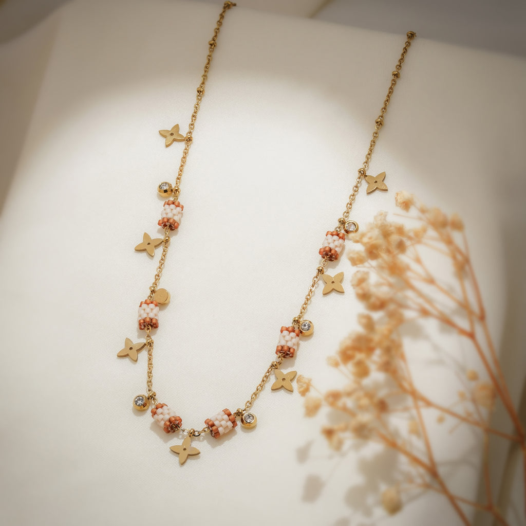 Angled view of gold chain with terracotta and white beaded barrels and brushed gold star charms