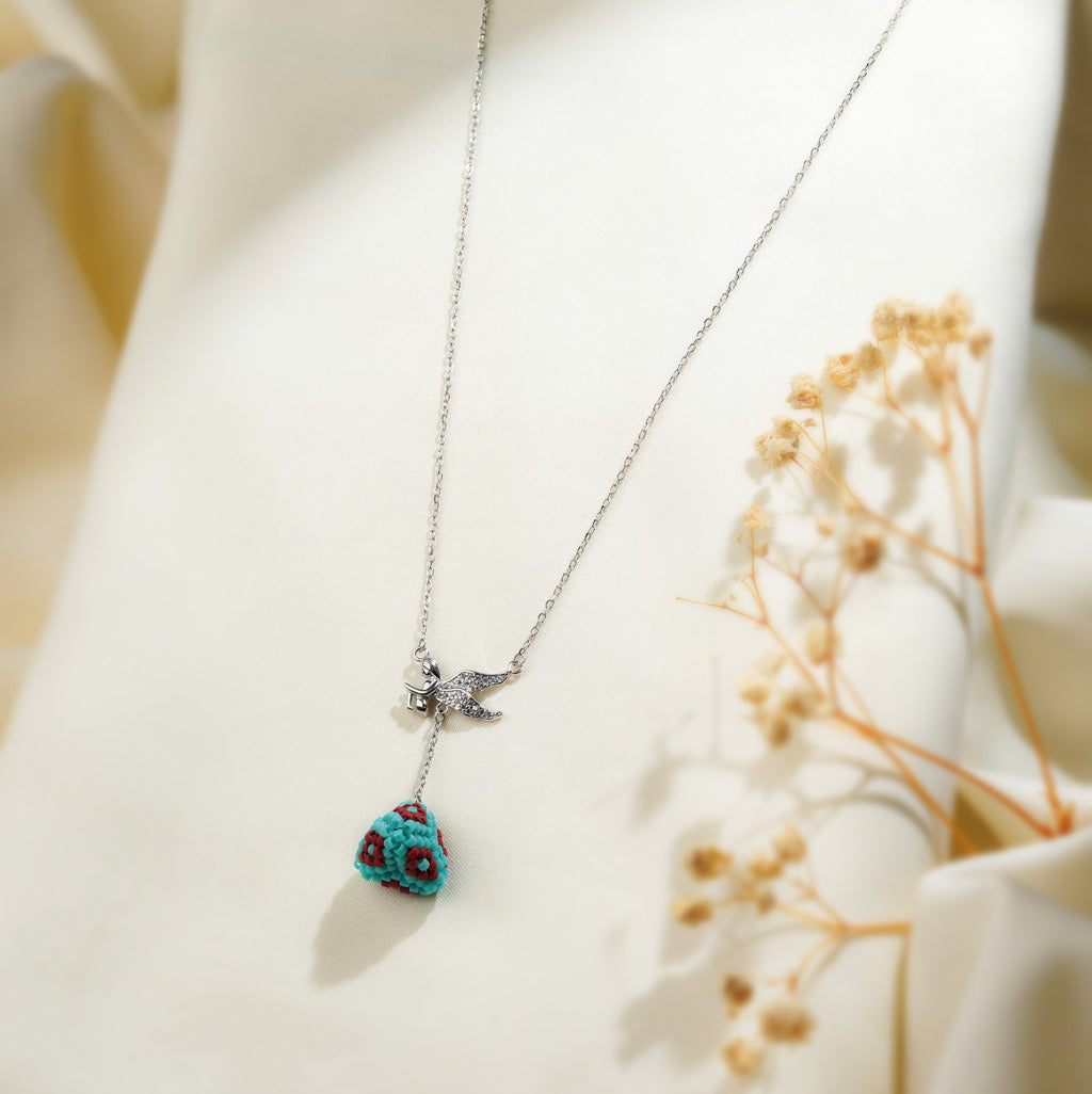 Close view of turquoise and red beaded pyramid drop below crystal angel wings on silver chain