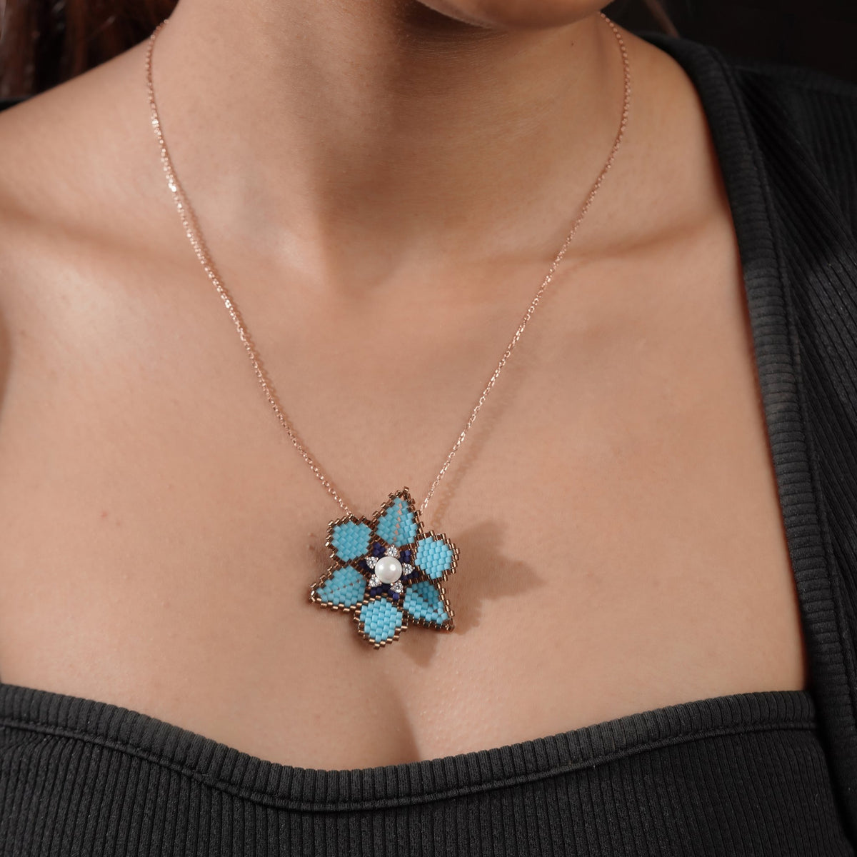 Model in a black top wearing a turquoise flower pendant on a rose-gold-tone chain
