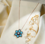 Turquoise beaded flower pendant on a rose-gold-tone chain draped over cream fabric