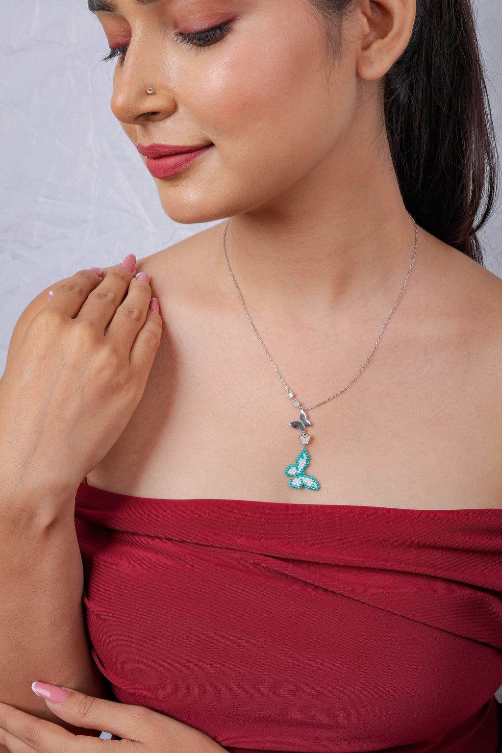 Model looking down, wearing the turquoise butterfly drop pendant on a silver chain