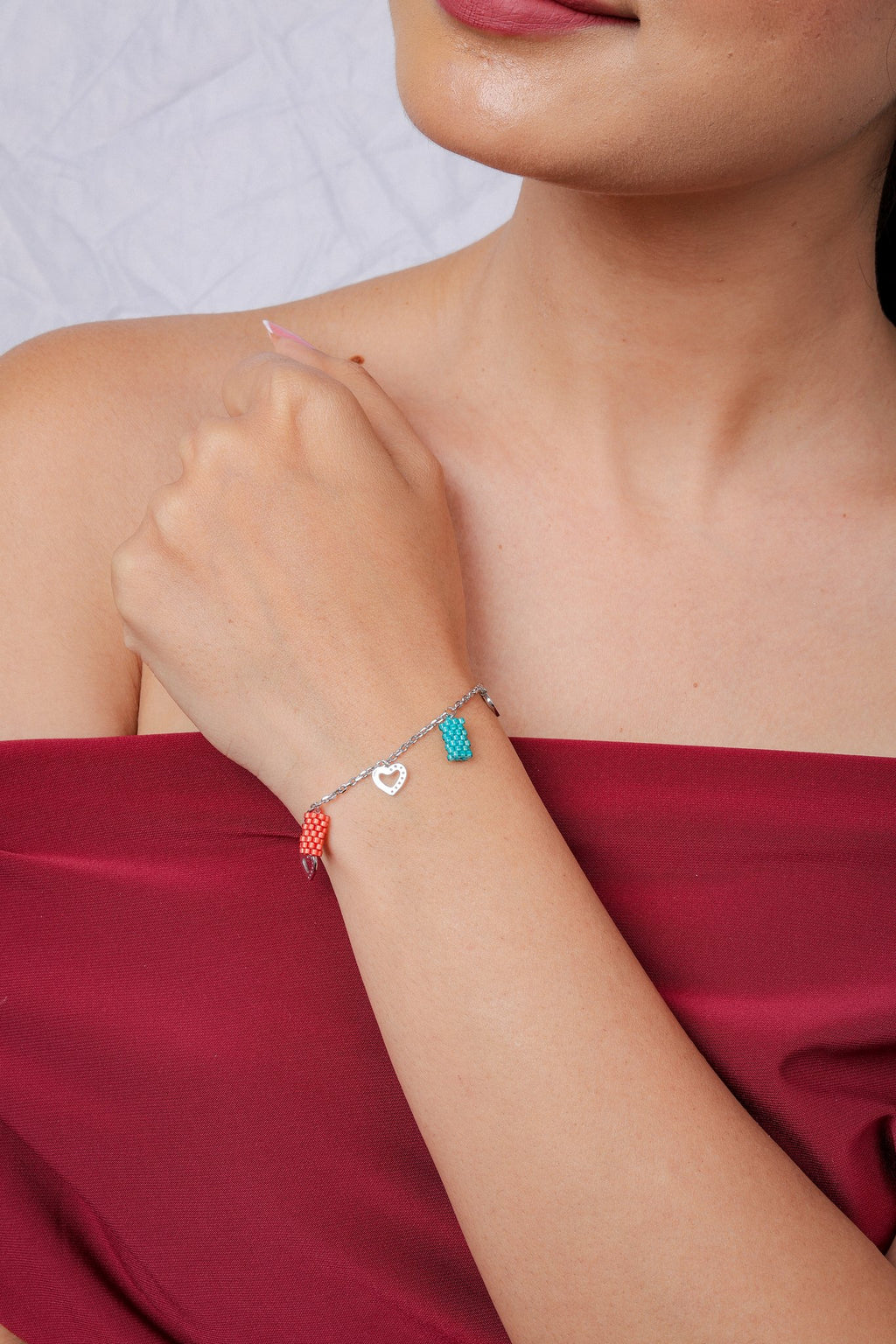 Turquoise and coral beaded charm bracelet worn at the wrist against a red top