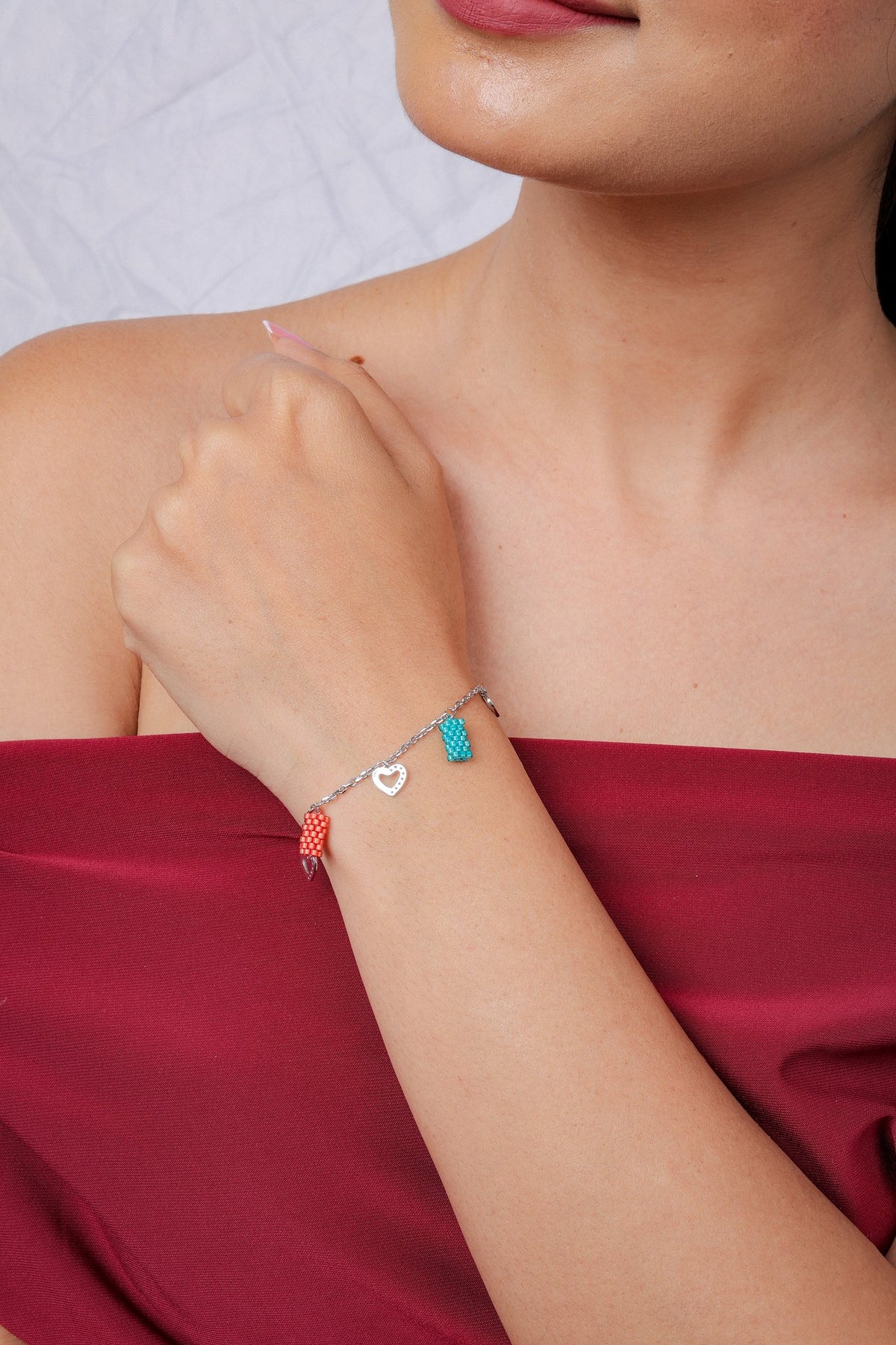Turquoise and coral beaded charm bracelet worn at the wrist against a red top