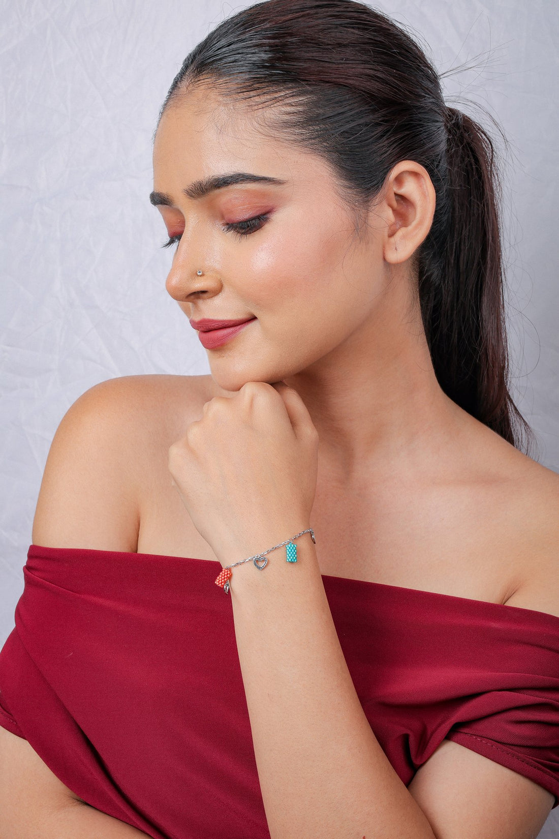 Turquoise and coral charm bracelet on a wrist, worn with a wine top