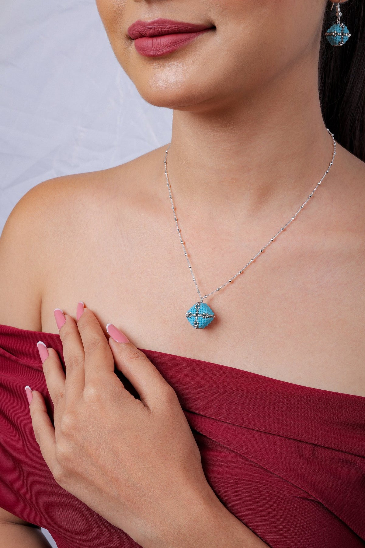 Turquoise beaded cube pendant on silver satellite chain with matching earring, worn by model