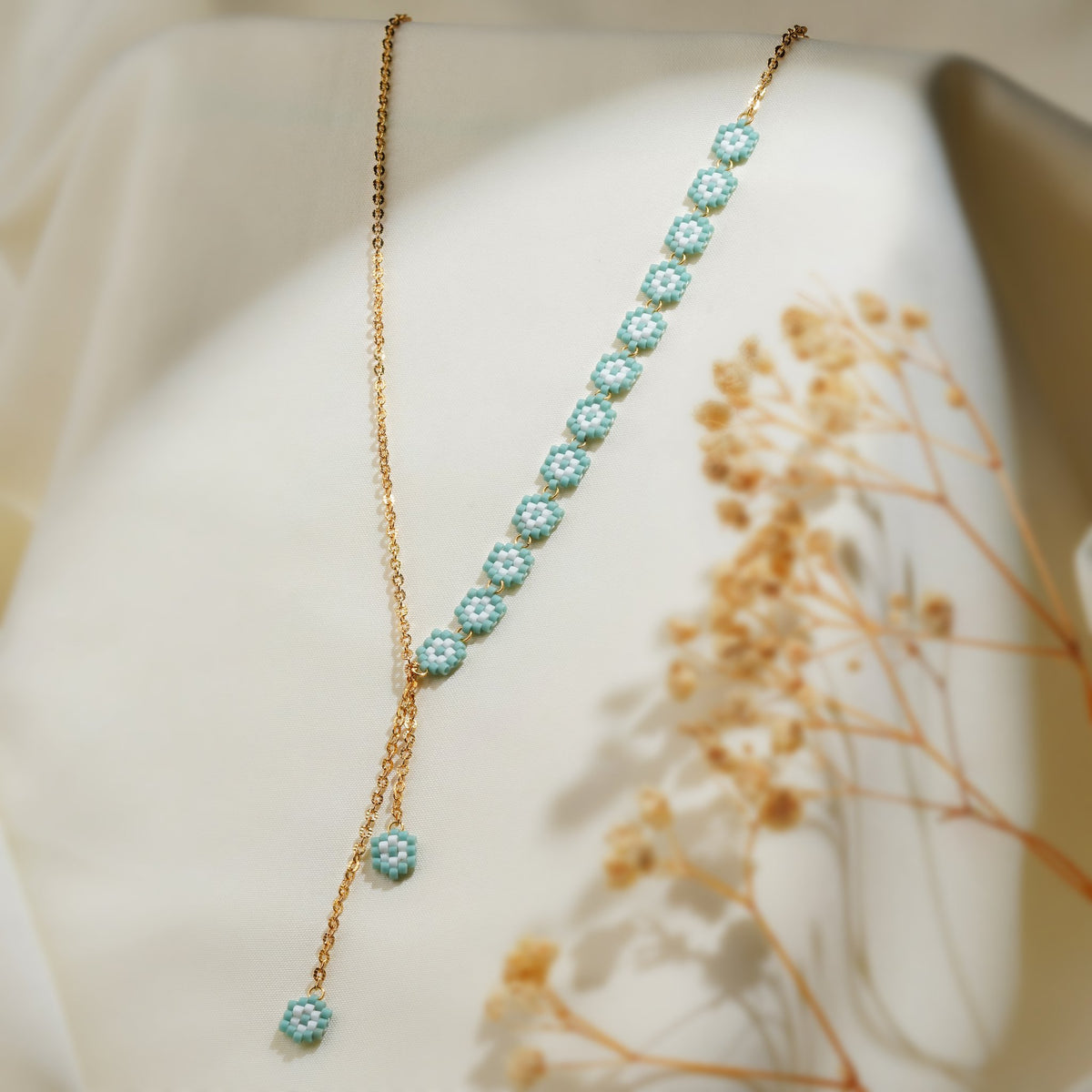 Gold-tone lariat necklace with a row of turquoise beaded daisies and two daisy drops