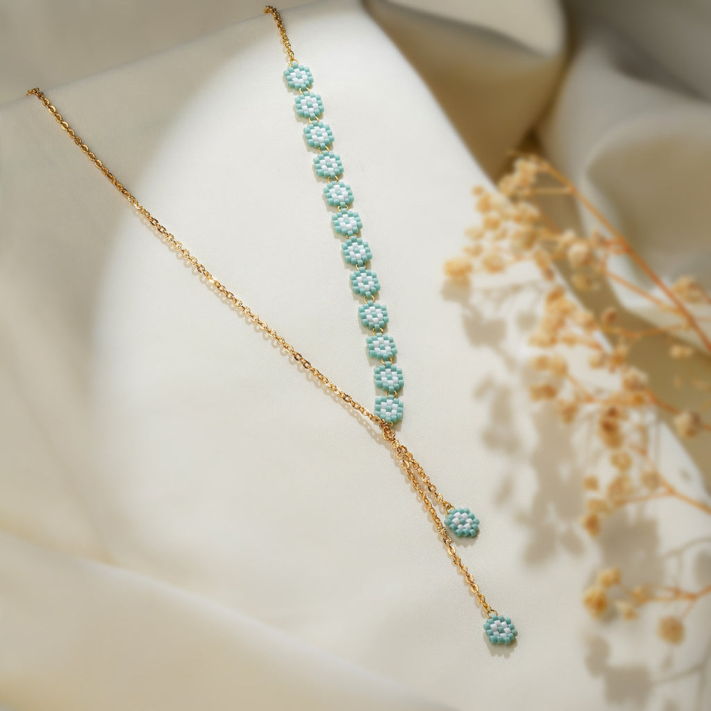 Turquoise beaded daisy lariat on a gold-tone chain draped over cream fabric