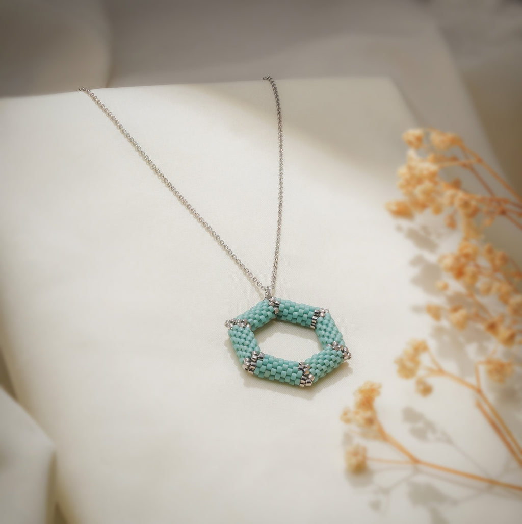 Open turquoise beaded hexagon pendant on a fine silver-tone chain over cream fabric