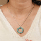 Turquoise hexagon pendant worn by a model in a cream V-neck sweater