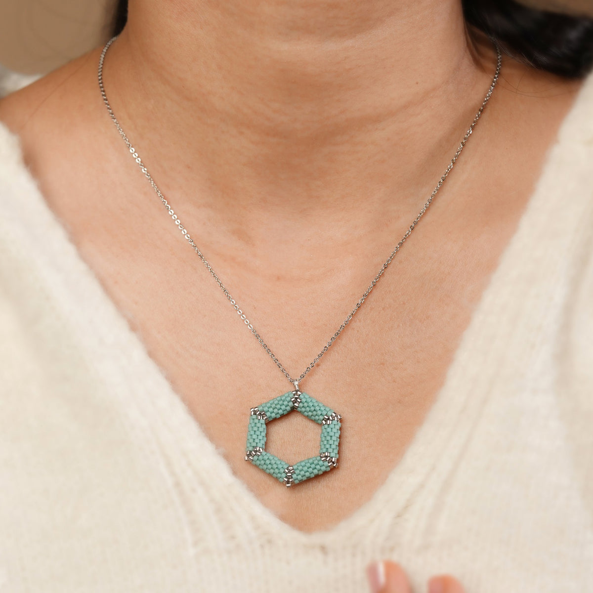 Turquoise hexagon pendant worn by a model in a cream V-neck sweater