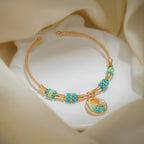 Gold-tone open bangle with turquoise striped bead barrels and a rose disc charm on white silk