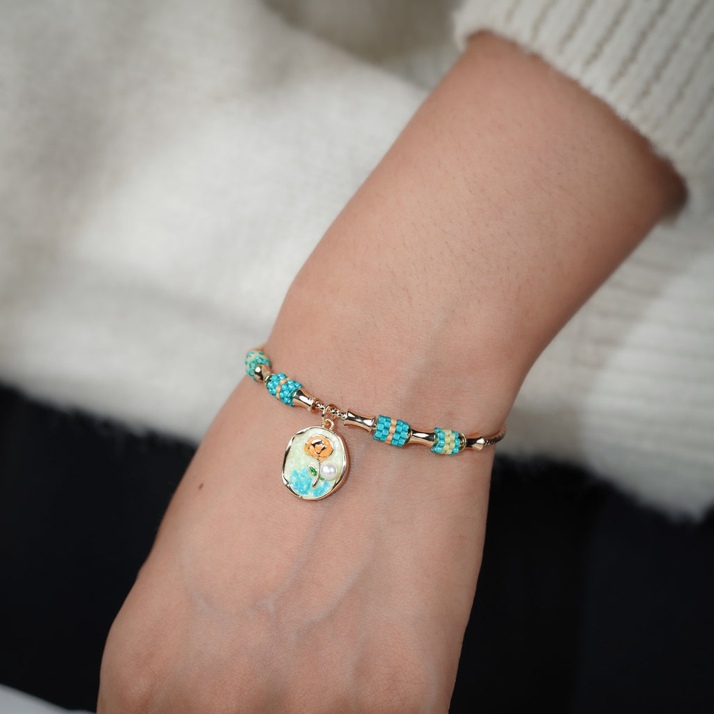Turquoise and gold-tone charm bangle worn on the wrist with a cream knit sleeve