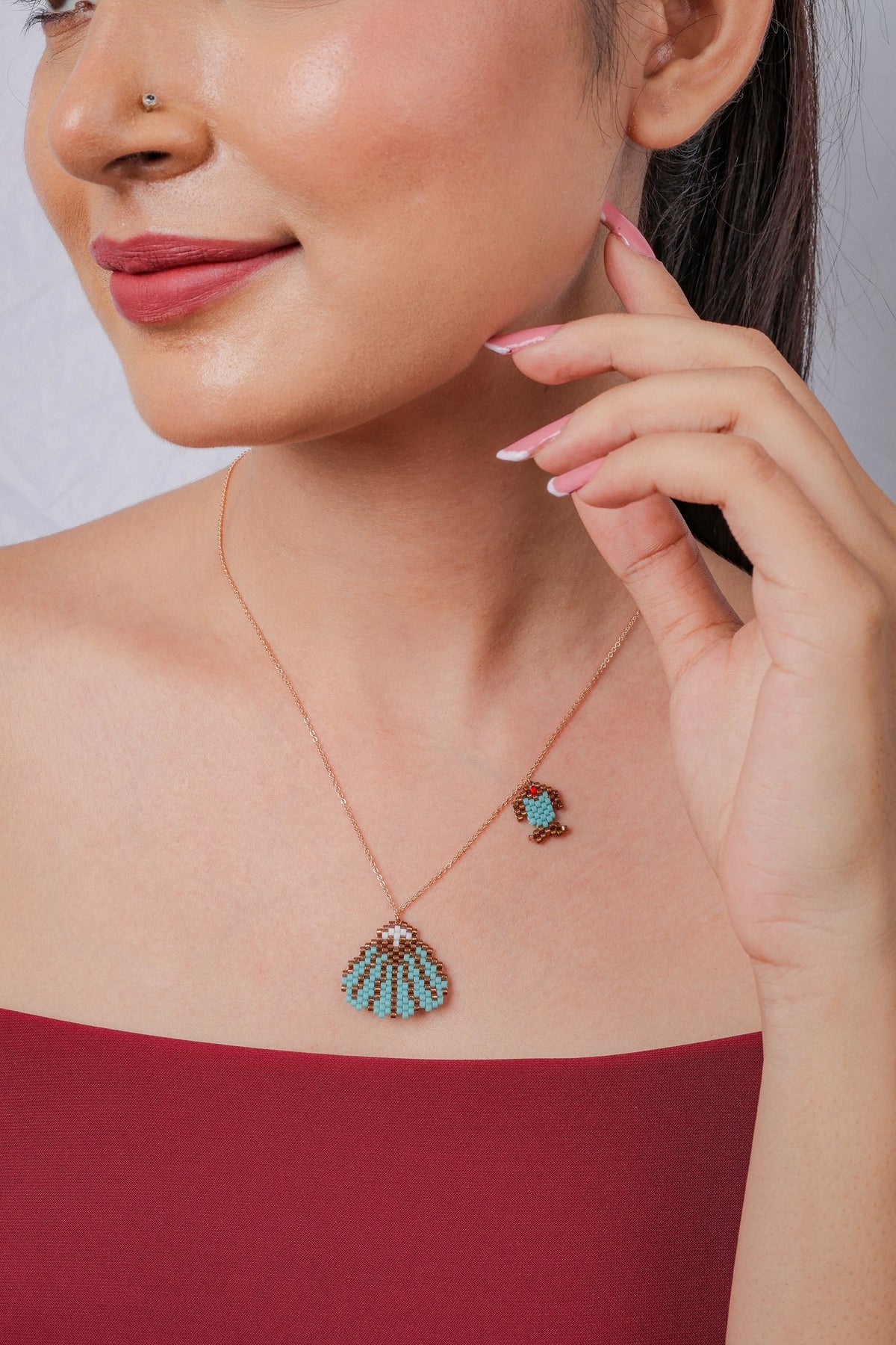 Rose-gold chain with a turquoise and bronze beaded seashell pendant and small beaded fish charm