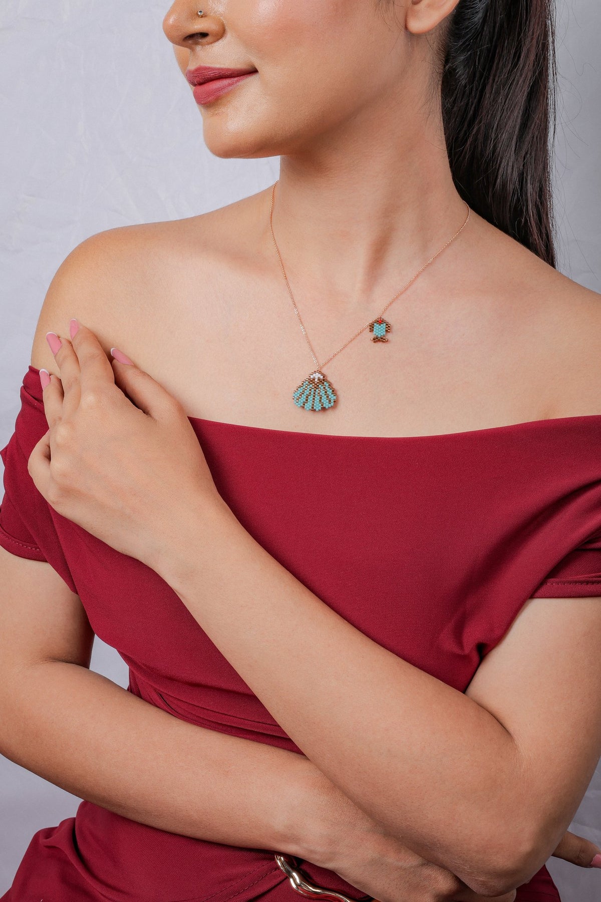 Model wearing rose-gold necklace with turquoise seashell pendant and fish charm