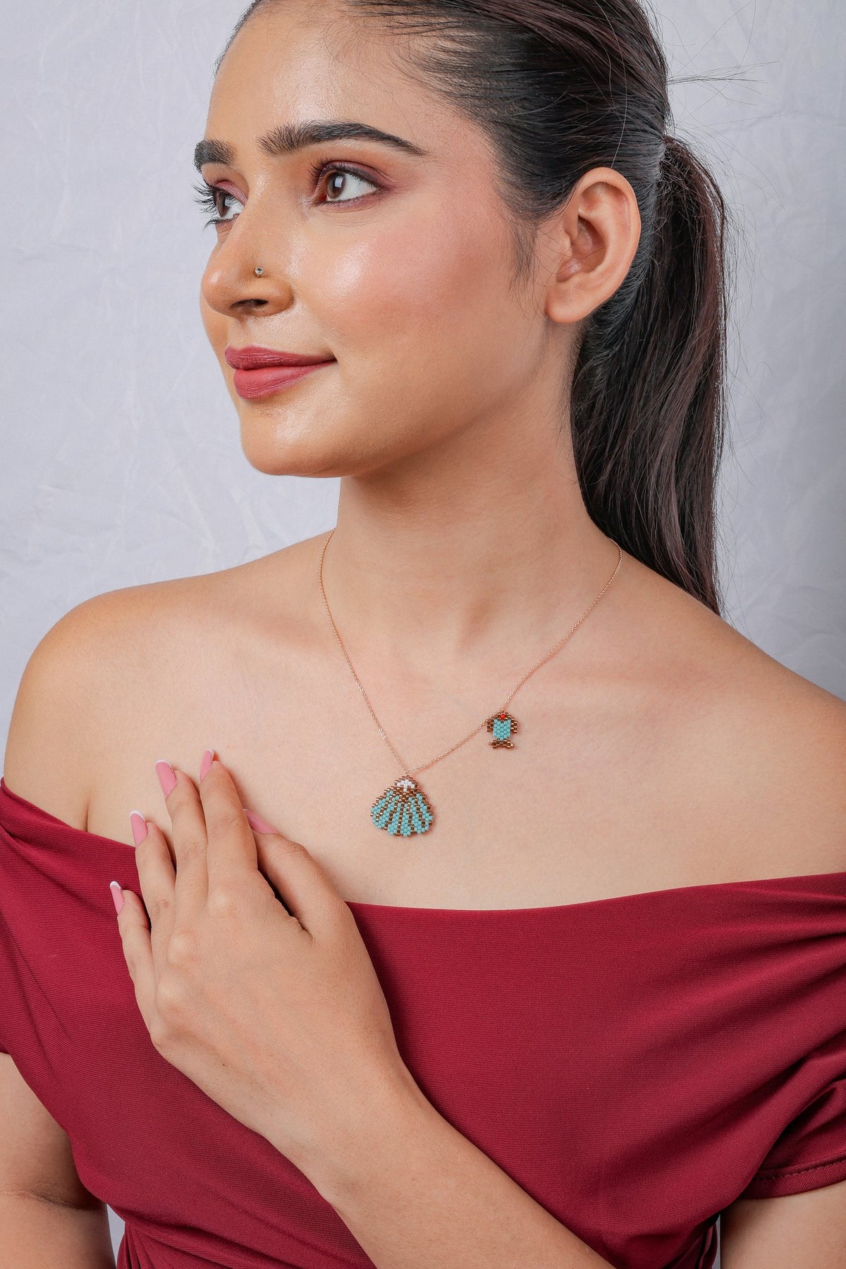 Model in profile wearing rose-gold chain with beaded seashell pendant and tiny fish