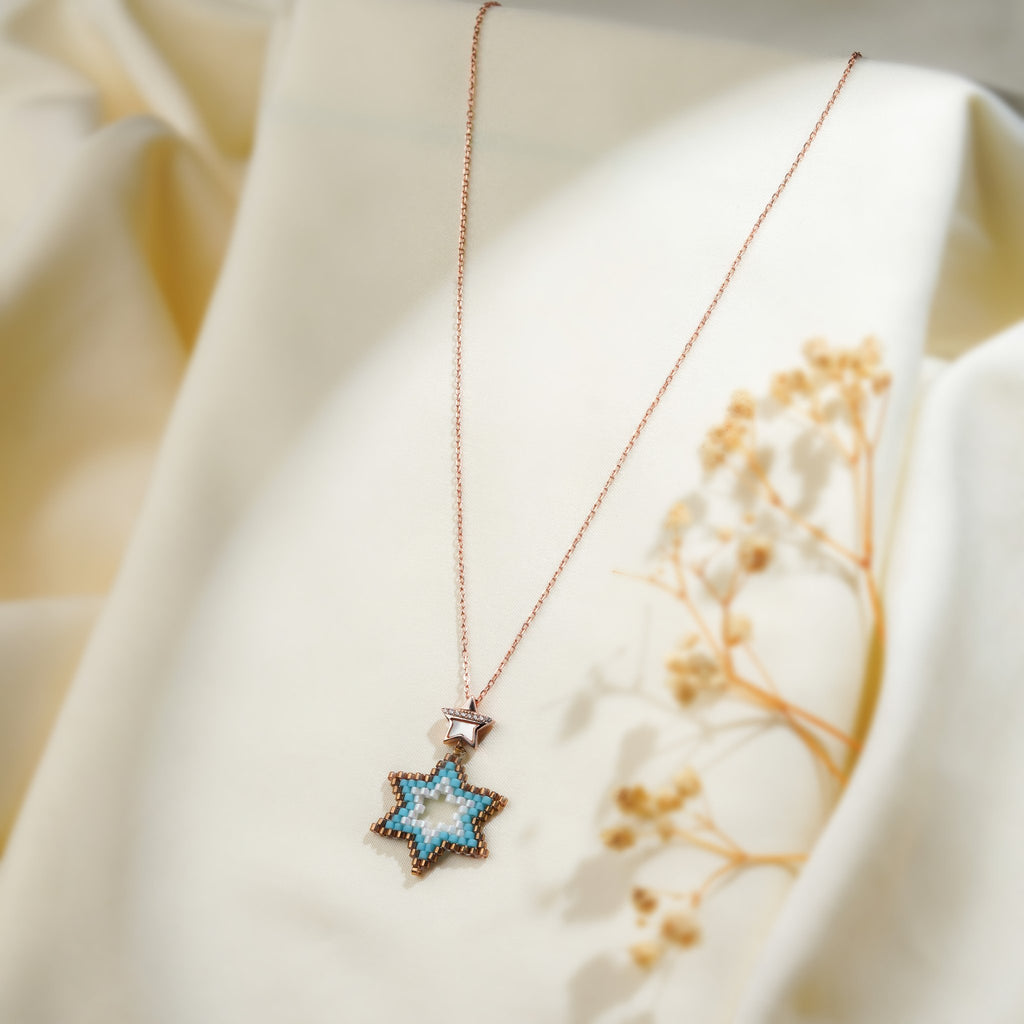 Angled view of turquoise beaded star pendant with pearly star bail on rose-gold chain