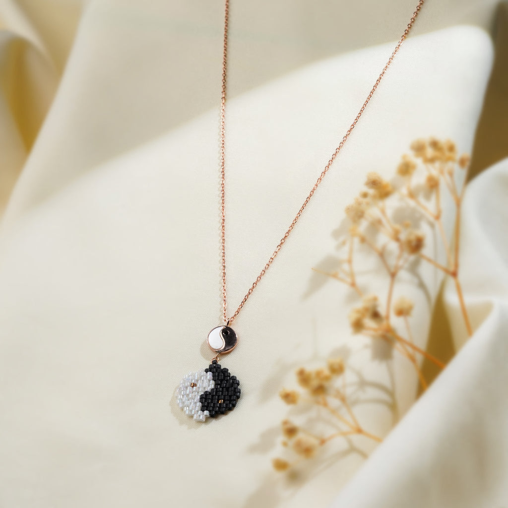 Rose-gold chain necklace with black and white beaded yin-yang pendant and small disc on cream silk